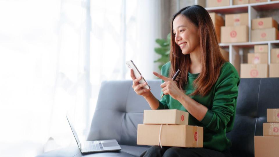 Happy transportation & Logistics customers looks at her smartphone while holding packages.